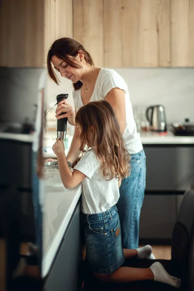 Mamãe e filha preparam a cereja para o pão de gengibre em sua cozinha doméstica. Bata com um liquidificador. A menina ajuda a mulher. — Fotografia de Stock