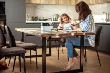 Genç, güzel anne ve tatlı kız birlikte bir mandala deseni çiziyorlar. Sanatsal kalemler ve renkli kalemler..