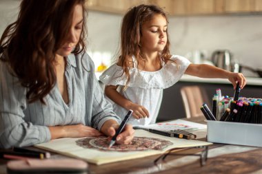 Genç, güzel anne ve tatlı kız birlikte bir mandala deseni çiziyorlar. Sanatsal kalemler ve renkli kalemler..