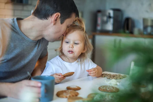 Papà e figlia decorano il pan di zenzero di Natale a casa. Un ragazzo e una ragazza dipingono con cornetti con la glassa di zucchero sui biscotti. Decorazione di anno nuovo, rami di un albero di Natale. — Foto Stock