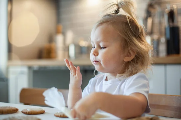 Pequena menina bonito decora pão de gengibre com açúcar de confeiteiro. Preparação para o conceito de Natal. — Fotografia de Stock