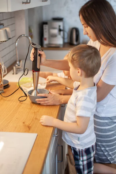 Mamãe e filha preparam a cereja para o pão de gengibre em sua cozinha doméstica. Bata com um liquidificador. A menina ajuda a mulher. — Fotografia de Stock