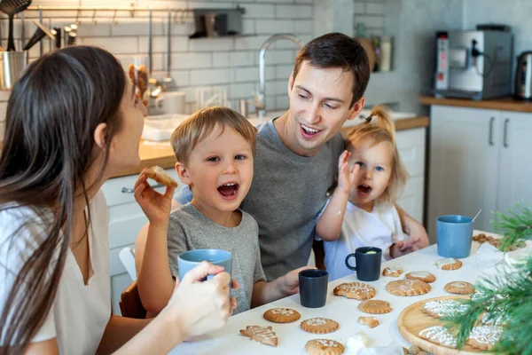 Uma família alegre decora pão de gengibre de Natal, bebe chá e se diverte. Elegante casa cozinha. — Fotografia de Stock