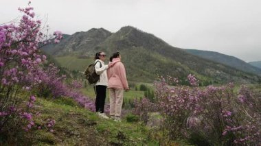 Two female tourists stand in the mountains in spring among blooming flowers and enjoy the beautiful views.