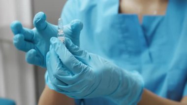 Mavi koruyucu eldivenlerle aşı şişesini hazırlayan doktorların yakın çekimi. İğne için. Hemşire içinde ilaç olan şişeyi sallıyor..