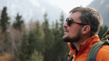 Turuncu ceketli bir erkek turistin yakın plan portresi çevreye bakar ve yürüyüş yaparken güzel manzaralara hayran kalır. Dağlarda yürüyüş..