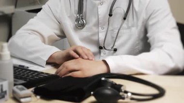 Beyaz önlüklü ve steteskoplu bir doktor modern bir klinikte bir hastayı muayene ediyor. Doktorların yakın plan resimleri masanın üzerinde gösteriliyor..