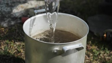 Dağ yürüyüşü sırasında metal bir tencereye dökülen temiz suyun yakın çekimi. Kamp yapma, açık hava yemekleri, seyahat yaşam tarzı ve doğada hayatta kalma kavramı..