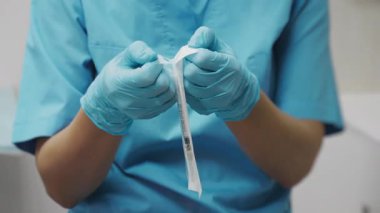 Temiz bir klinikte enjekte edilmeden önce mavi üniformalı ve eldivenli hemşirenin steril şırıngayı açmasına yakın durun..