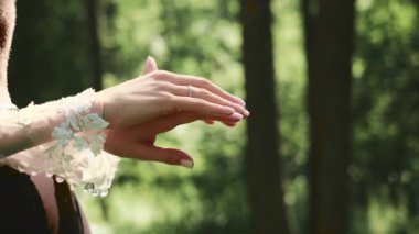 Düğün günü zarif dantelli kollarıyla gelin ellerini kapat. Güneş ışığında yeşil ağaçların altında hassas bir jest. Doğada romantik bir an..