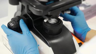 Mavi eldivenli bilim adamlarının ellerini kapatın. Mikroskop merceklerini yerleştirin. Kan analiz laboratuvarında tıbbi teşhisler ve araştırmalar için..