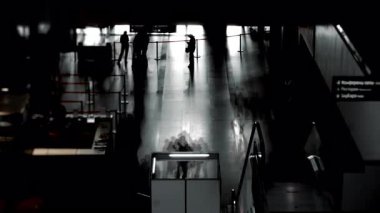 Dinamik zaman atlaması, geniş modern bir salonda yürüyen insanların siluetlerini gösteriyor, yerde yansımalar ve hareket bulanıklığı yaratıyor, yapay ışığın altında..