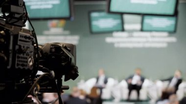 İş konferansı sırasında arka planda bulanık katılımcılar ve sunum ekranlarıyla profesyonel kamera kayıt panelini kapat.