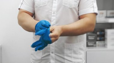 Parlak klinikte prosedürden önce mavi nitrile eldiven takan erkek doktorlara yakından bakın. Sağlık güvenliğine ve işyerindeki steril korumaya odaklanın..