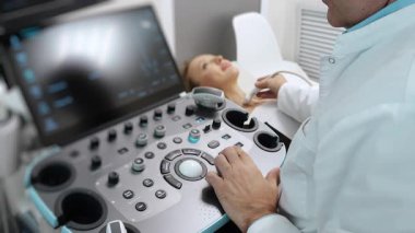 Modern tıp kliniğindeki kadın hastalara tiroid bezi taraması yaparken doktor ultrason cihazı çalışıyor. Sağlık teknolojisi ve klinik görüntüleme süreci..