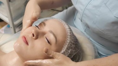 Güzellik kliniğinde cilt bakımı sırasında kadın yüzüne krem sürüp masaj yapıyor. Cilt sağlığı için güzellik tedavisi.