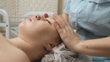 Profesyonel kozmetik uzmanı cilt kremi ile yüz masajı yapıyor ve güzellik kliniğinde gençleştirme tedavisi uyguluyor..