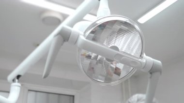 Diş hekimi, sözlü muayeneden önce parlak LED diş lambasını ayarlıyor, modern diş kliniğinde el ve ışık ekipmanlarını kapatıyor.