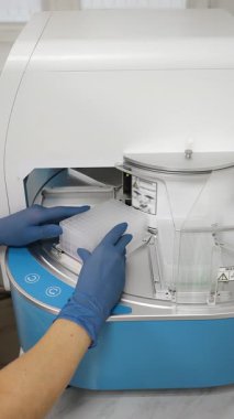 Bilim adamı 96 kuyu levhasını modern laboratuardaki otomatik PCR çalışma istasyonuna yüklüyor..