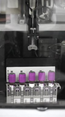 Modern bir tıp laboratuarı ortamında klinik teşhisler için kullanılan örnek iğnesi mor kapaklı kan tüplerini kullanan otomatik bir laboratuvar analizcisinin dikey görüntüsü..