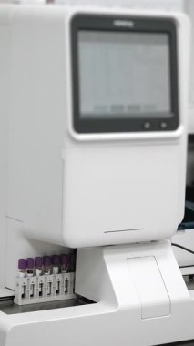 Modern bir klinik tanı laboratuarında çoklu test tüplerini işleyen otomatik bir laboratuvar kan analizcisinin dikey yakın çekimi..