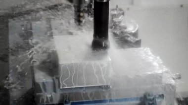 CNC değirmen makinesi endüstriyel fabrikada hassas işlemler sırasında soğutucu sıvı ve metal çiplerle metal blokları kesiyor..
