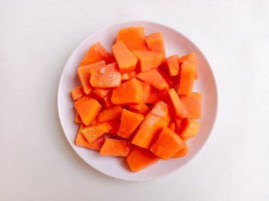 Beyaz bir tabakta altın çatalla servis edilen taze papaya küpleri. Sağlıklı gıda konsepti, temiz arka plan, doğal ışık, tropikal meyve düzlüğü