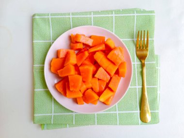 Beyaz bir tabakta altın çatalla servis edilen taze papaya küpleri. Sağlıklı gıda konsepti, temiz arka plan, doğal ışık, tropikal meyve düzlüğü