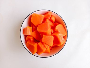 Beyaz bir tabakta altın çatalla servis edilen taze papaya küpleri. Sağlıklı gıda konsepti, temiz arka plan, doğal ışık, tropikal meyve düzlüğü