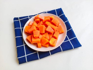 Beyaz bir tabakta altın çatalla servis edilen taze papaya küpleri. Sağlıklı gıda konsepti, temiz arka plan, doğal ışık, tropikal meyve düzlüğü