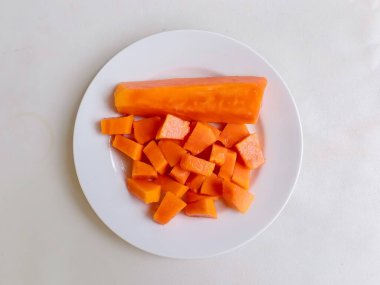 Beyaz bir tabakta altın çatalla servis edilen taze papaya küpleri. Sağlıklı gıda konsepti, temiz arka plan, doğal ışık, tropikal meyve düzlüğü