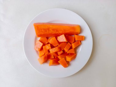 Beyaz bir tabakta altın çatalla servis edilen taze papaya küpleri. Sağlıklı gıda konsepti, temiz arka plan, doğal ışık, tropikal meyve düzlüğü