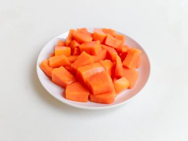 Beyaz bir tabakta altın çatalla servis edilen taze papaya küpleri. Sağlıklı gıda konsepti, temiz arka plan, doğal ışık, tropikal meyve düzlüğü