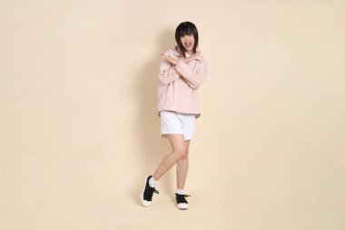 Pembe ultraviyole koruyucu kapüşonlu ceket giyen genç Asyalı kadın bej arka plana hayır, güneş koruma giysisine hayır diyor..