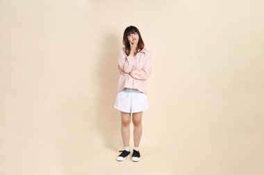 Pembe ultraviyole koruyucu kapüşonlu ceket giyen genç Asyalı kadın bej arka plan, güneş koruma giysisi konseptine karşı düşünüyor..