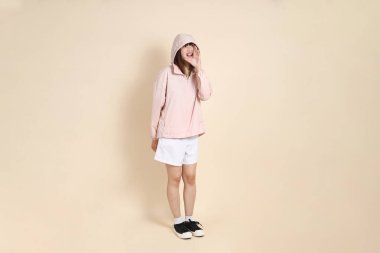 Pembe ultraviyole koruyucu kapüşonlu ceket giyen genç Asyalı kadın bej arka plan, güneş koruması kıyafet konseptine karşı bağırıyor..