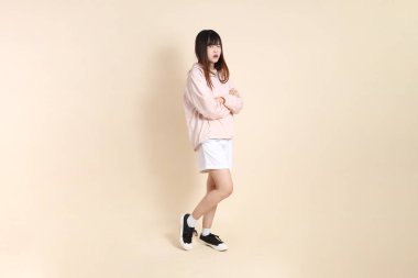 Pembe ultraviyole koruyucu kapüşonlu ceket giyen genç Asyalı kadın bej arka planda kızgın ve çığlık atıyor, güneş koruma giysisi konseptine karşı..