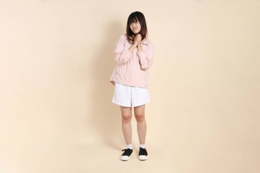 Pembe ultraviyole koruyucu kapüşonlu ceket giyen genç Asyalı kadın bej arka planda etkileyici, güneş korumalı giysi konsepti.