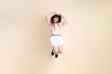 Pembe ultraviyole koruyucu kapüşonlu ceket giyen genç Asyalı bir kadın bej arka plana atlıyor, güneş korumalı giysi konseptine atlıyor..