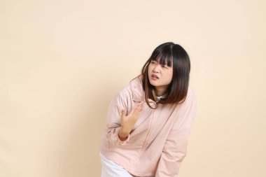 Pembe ultraviyole koruyucu kapüşonlu ceket giyen genç Asyalı bir kadın bej arka plan ve güneş koruma giysisi kavramına karşı sıcak hissediyor..