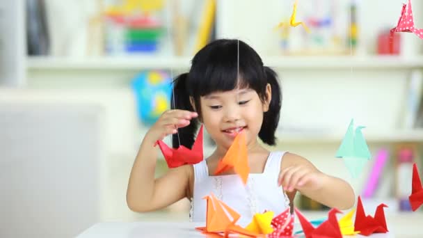 Милая девушка играет в бумажных журавликах в помещении — стоковое видео