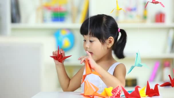Chica encantadora jugando grúas de papel interior — Vídeos de Stock