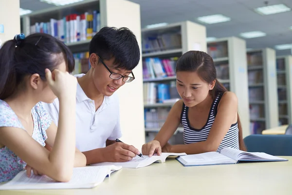 Jóvenes estudiantes universitarios estudian juntos en la biblioteca — Foto de Stock