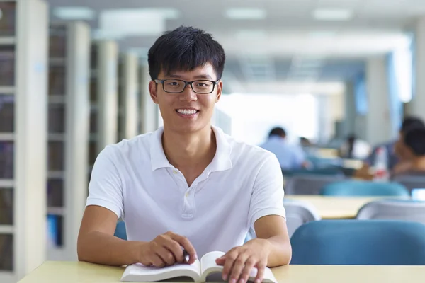 Unga manliga collegestudent tittar på kameran leende i bibliote — Stockfoto