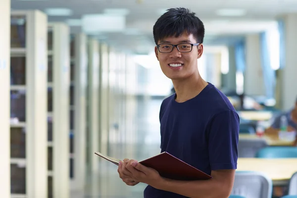 Junger männlicher College-Student blickt in die Bibliothek und lächelt in die Kamera — Stockfoto