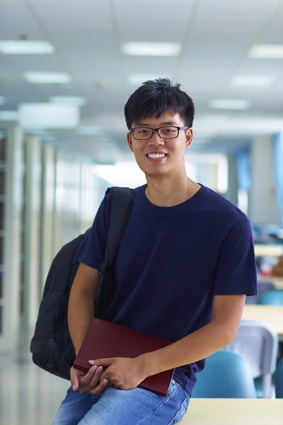 Unga manliga collegestudent tittar på kameran leende i bibliote — Stockfoto