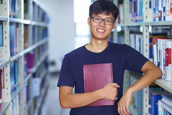 Jonge mannelijke college student op zoek op camera glimlach in de librar — Stockfoto