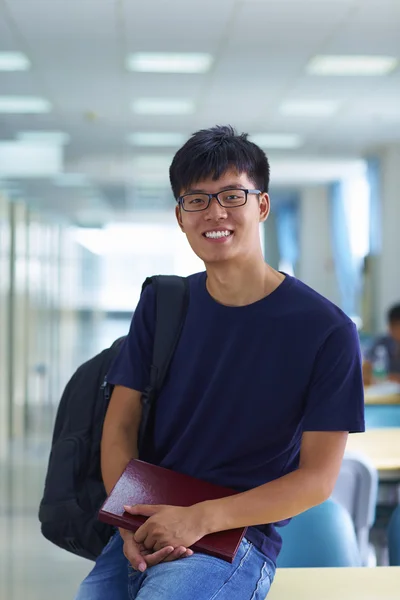 Junger männlicher College-Student blickt in die Bibliothek und lächelt in die Kamera — Stockfoto