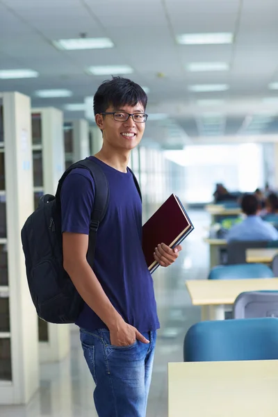 Unga manliga collegestudent tittar på kameran leende i bibliote — Stockfoto