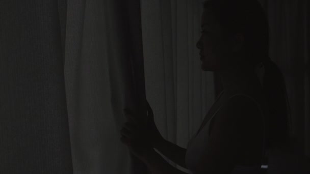 Νεαρή γυναίκα ανοίγει την κουρτίνα κοιτάζοντας έξω γελώντας απολαμβάνοντας — Αρχείο Βίντεο
